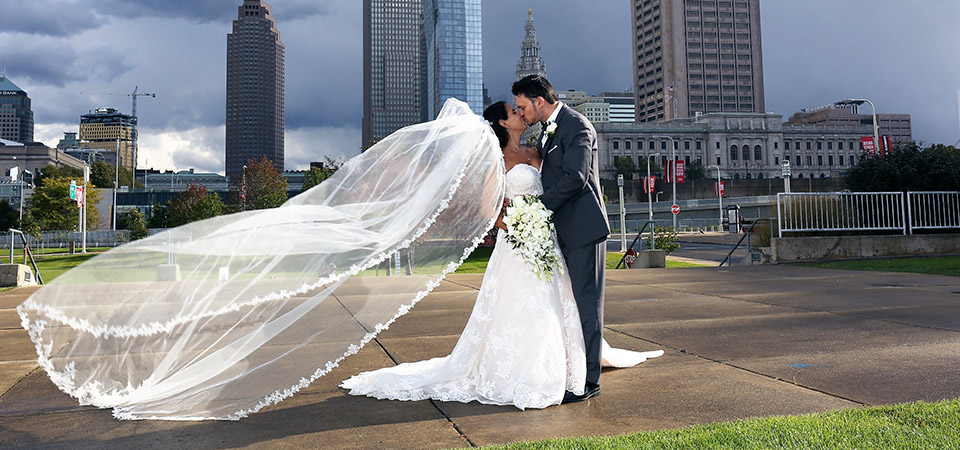 Photo of a bride and groom sharing a kiss with downtown Cleveland in the background.